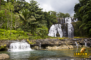 View of Situbo Falls from a distance with a small cascade over interesting rock formations