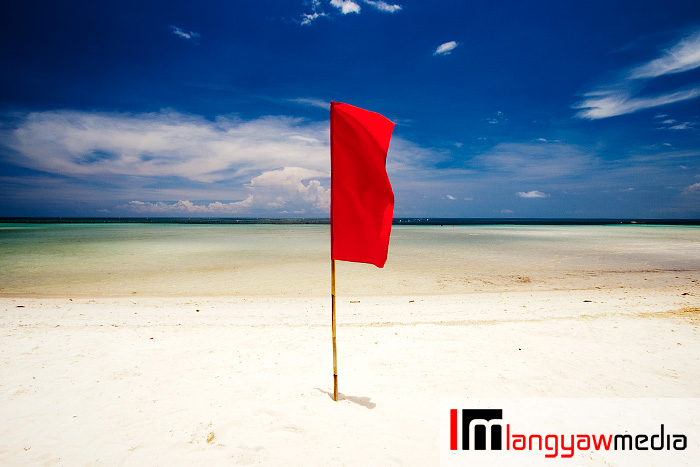 Red flag stand guard at the white sand beach