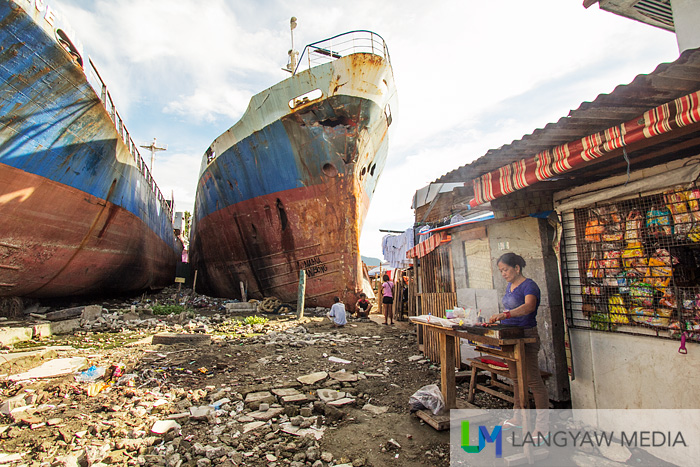 An entrepreneurial woman sells grilled food with the ships at the backgroun in Anibong District