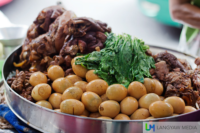 A khao kha mu vendor's cart filled with boiled eggs, boiled water spinach, mushrooms and the stewed pork leg