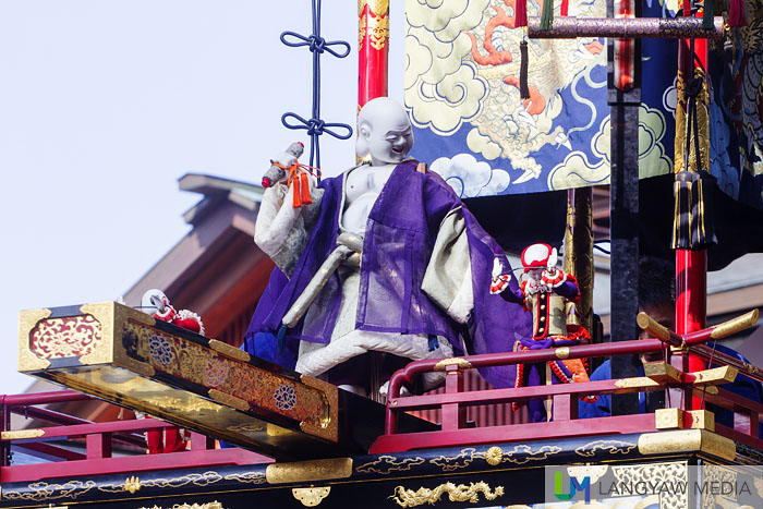 The Priest Hotei as a puppet with two other puppets atop the Hoteitai yatai at the square below the shrine. Skilled puppeters operate these three during the twice a day performance on October 9 and 10.