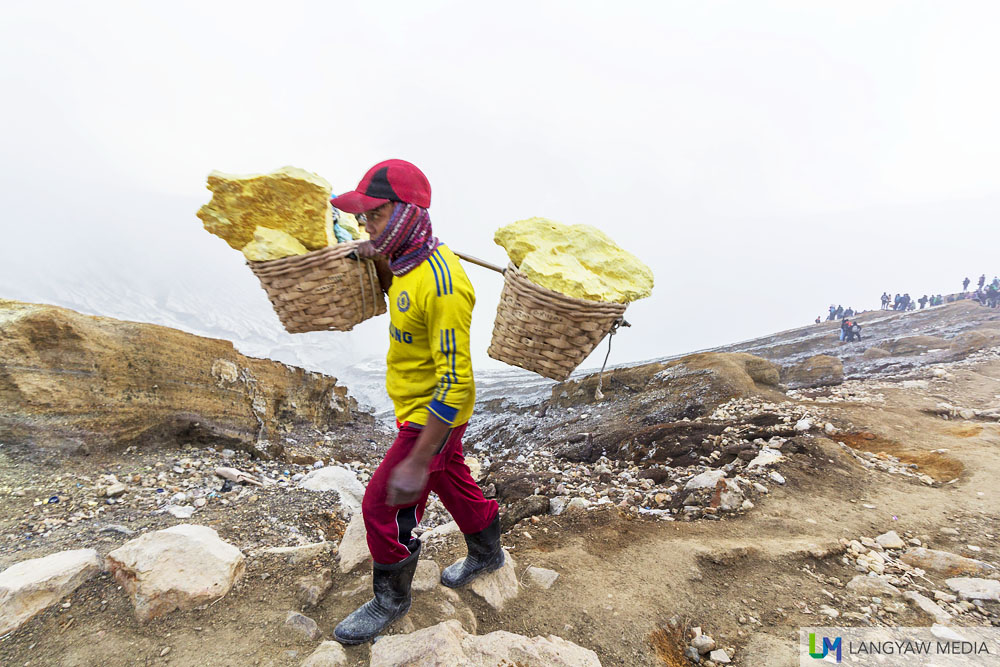 A sulphur miner carrying blocks of the element from the crater below